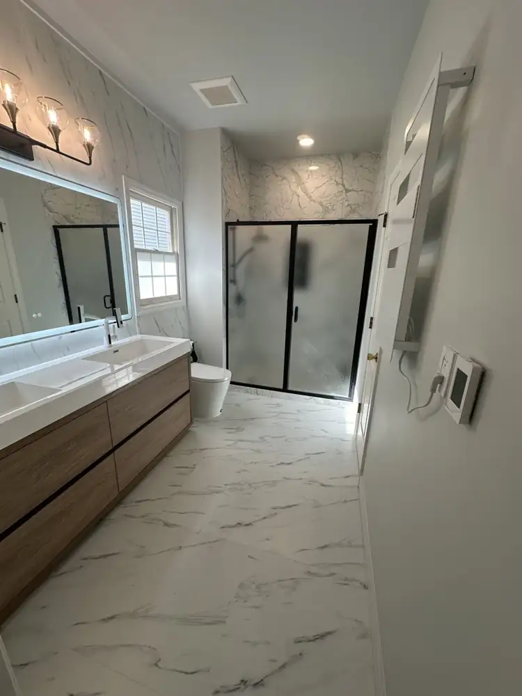 Bathroom with marble-look porcelain floor and feature wall, wood double vanity, lighted mirror and black-framed shower, Aurora, Ohio