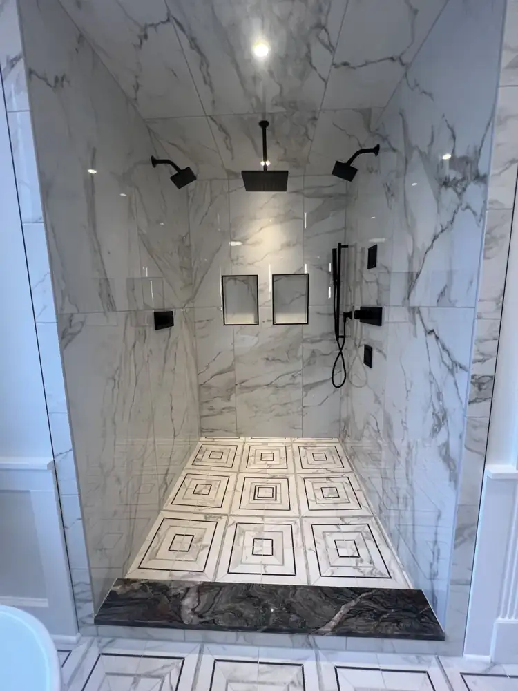 Walk-in shower with three black shower heads, marble-look porcelain walls and ceiling, geometric floor and stone curb, Ohio