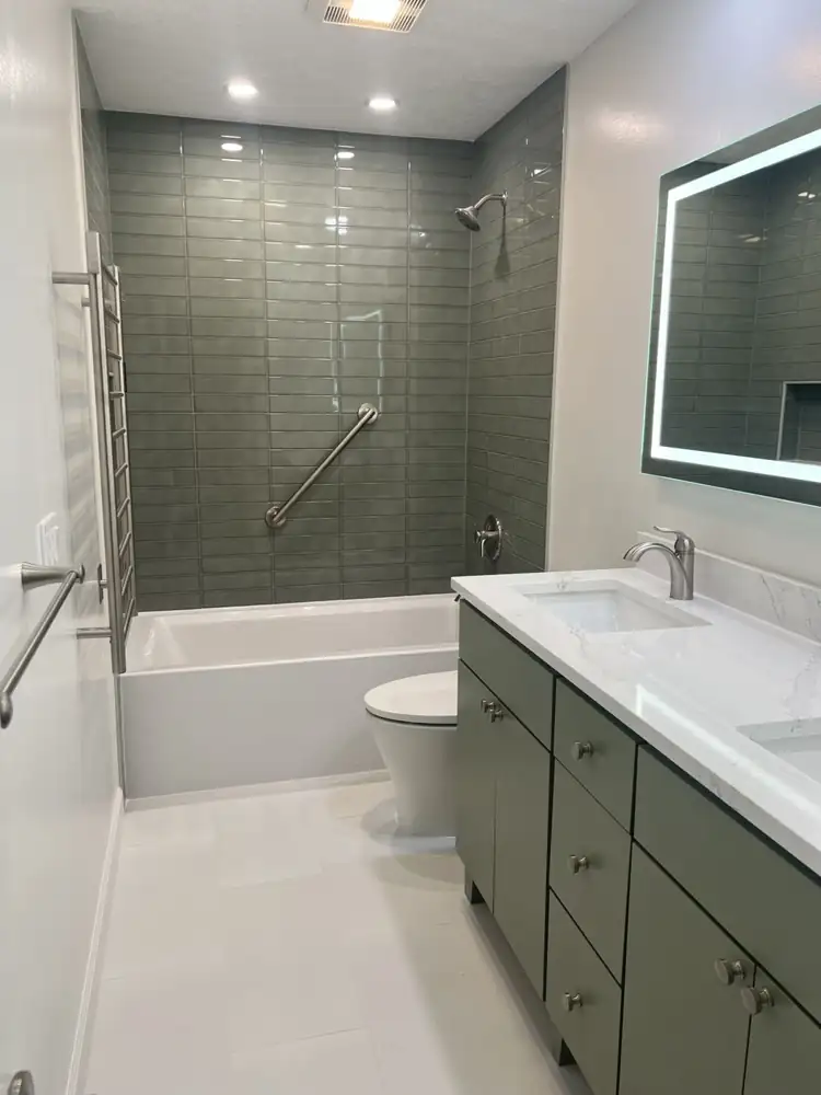 Bathroom with sage green glass tile tub surround, grab bar, heated towel rack and green vanity with quartz top, Brecksville, Ohio