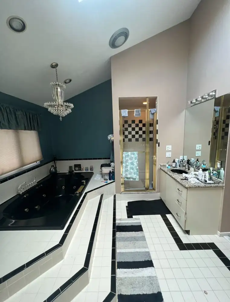 1990s primary bathroom with black jetted tub on tiled platform and brass shower door before remodel, Beachwood, Ohio