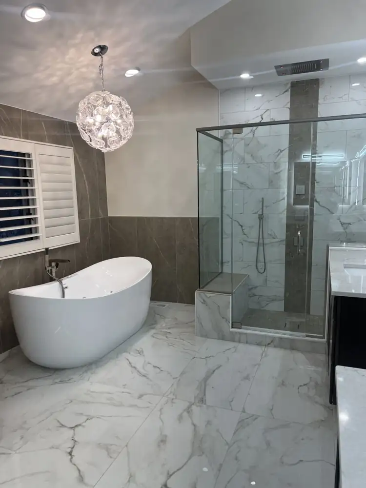 Another view: Primary bathroom with freestanding tub, glass chandelier, frameless glass shower with ceiling rain head and body jets, marble-look floor, Beachwood, Ohio