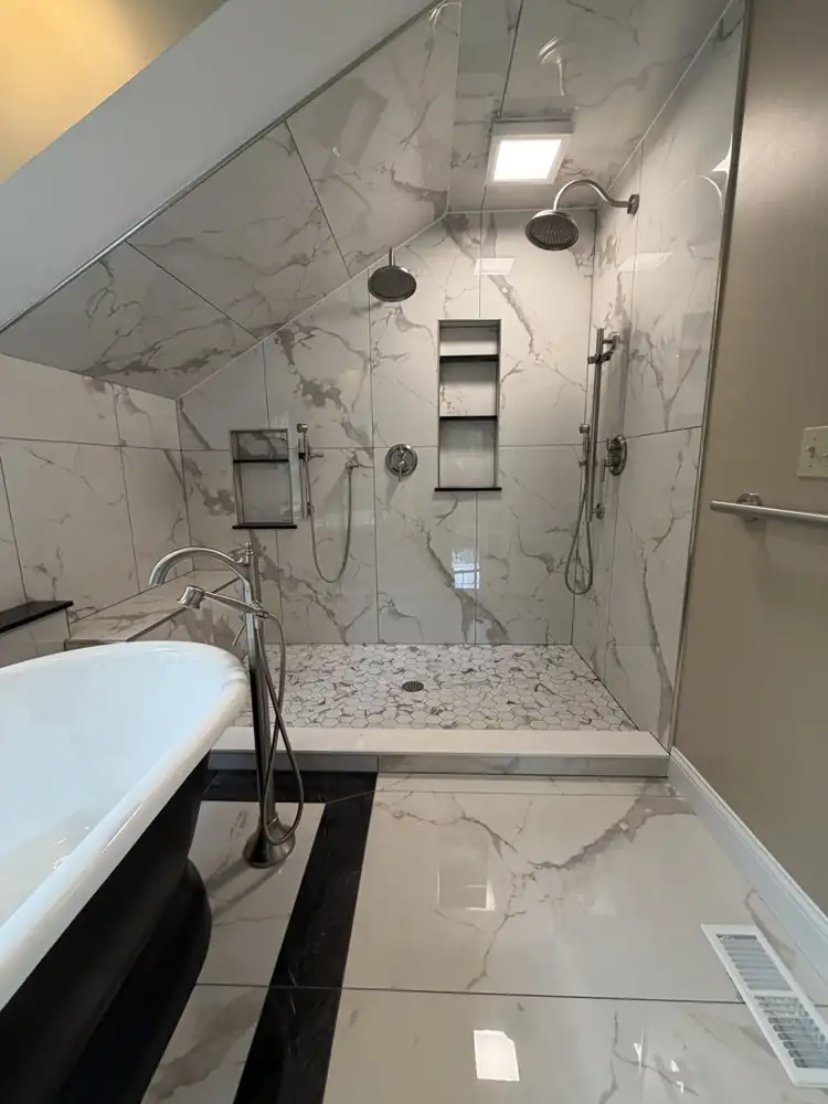 Another view: Black pedestal tub on a black-bordered marble-look tile inset under a dormer window, walk-in shower with bench, Chagrin Falls, Ohio