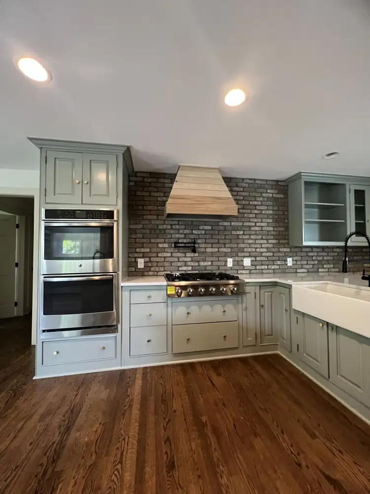 Gas cooktop under a custom wood range hood with brick backsplash and pot filler