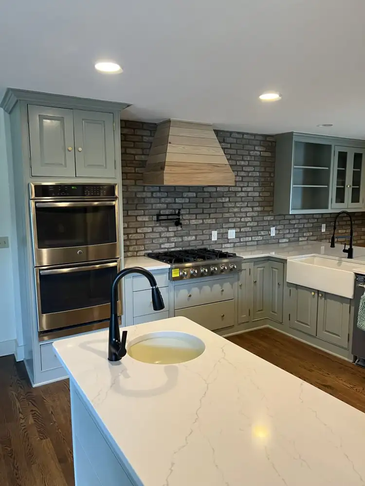 Another view: Kitchen with sage green cabinets, brick backsplash, wood range hood, quartz counters and farmhouse sink, Hudson, Ohio