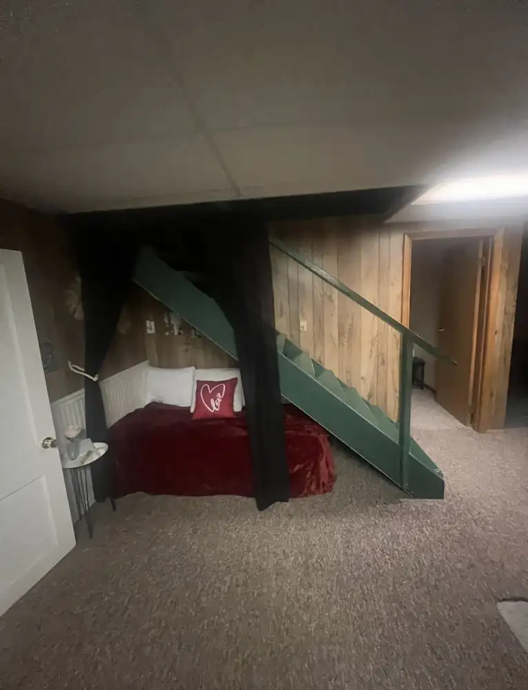 Dated basement with wood paneling, drop ceiling, carpet and open green staircase before remodel, Mantua, Ohio