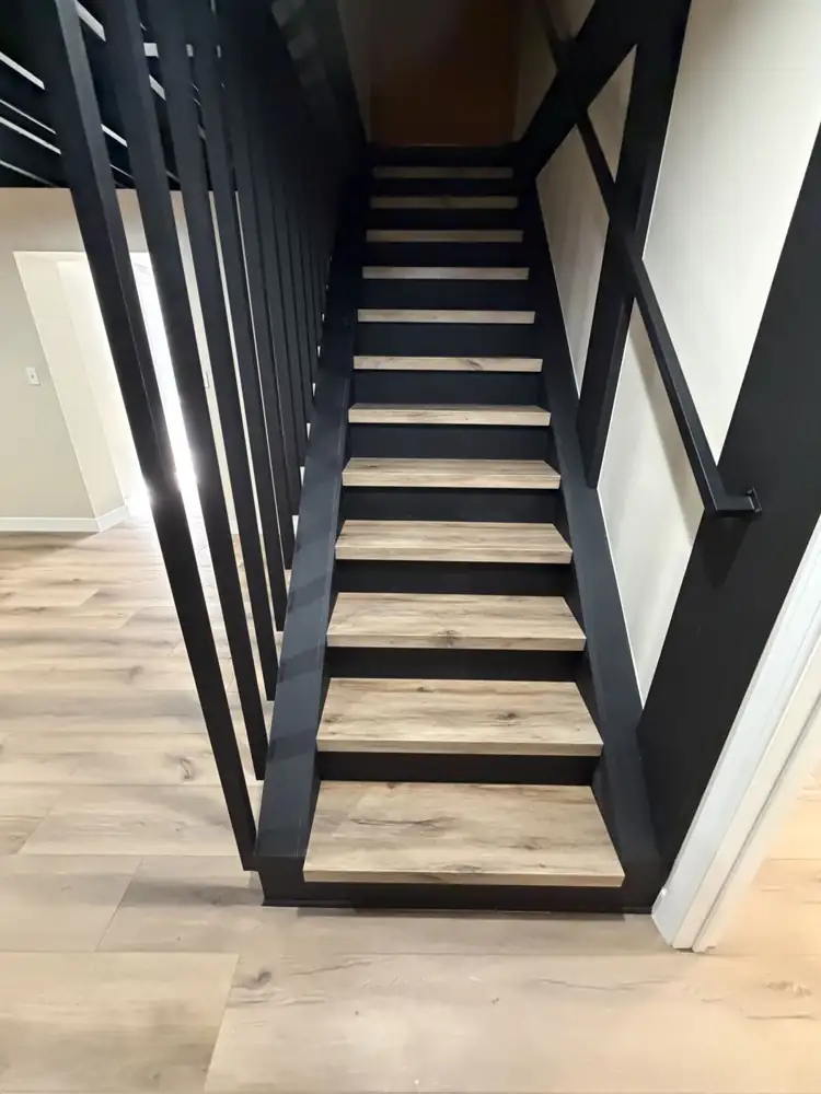 Another view: Rebuilt basement staircase painted black with slatted wall, wood-look treads, black open ceiling and plank flooring, Mantua, Ohio