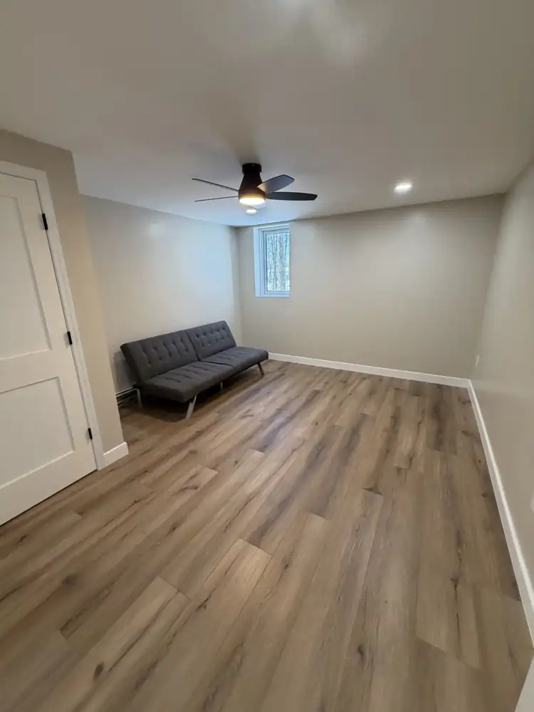 Another view: Rebuilt basement staircase painted black with slatted wall, wood-look treads, black open ceiling and plank flooring, Mantua, Ohio