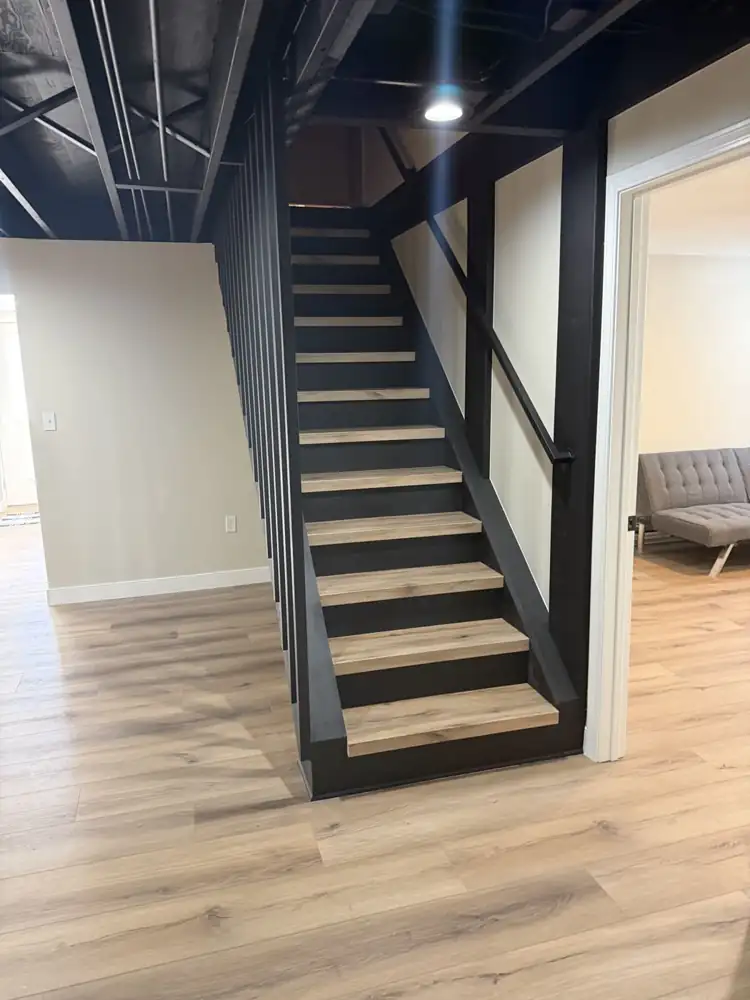 Another view: Rebuilt basement staircase painted black with slatted wall, wood-look treads, black open ceiling and plank flooring, Mantua, Ohio