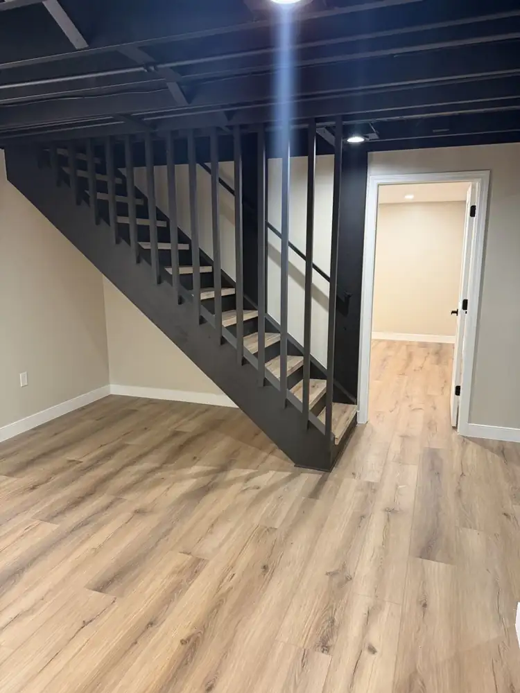 Another view: Rebuilt basement staircase painted black with slatted wall, wood-look treads, black open ceiling and plank flooring, Mantua, Ohio