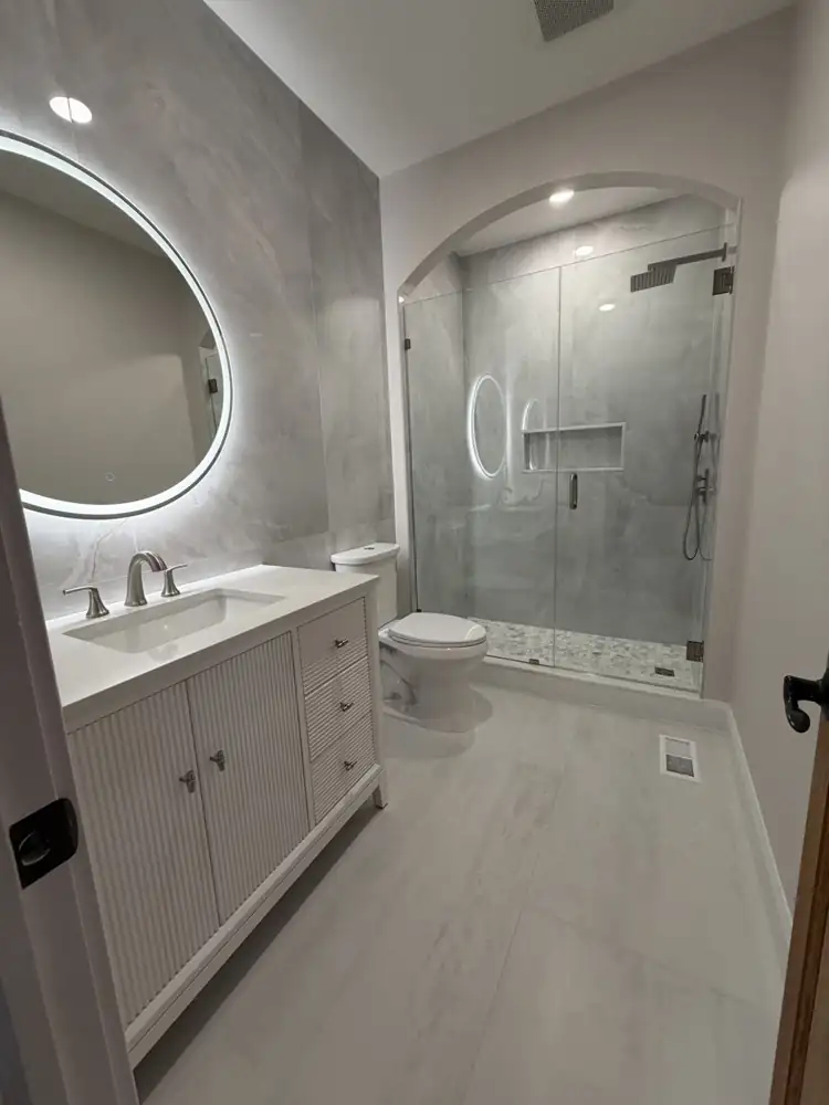 Bathroom with arched walk-in shower, large-format porcelain, round lighted mirror and fluted vanity, Mentor, Ohio