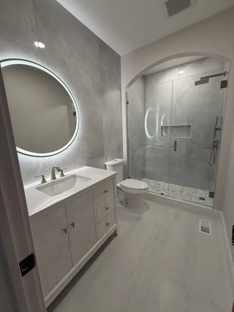 Another view: Bathroom with arched walk-in shower, large-format porcelain, round lighted mirror and fluted vanity, Mentor, Ohio