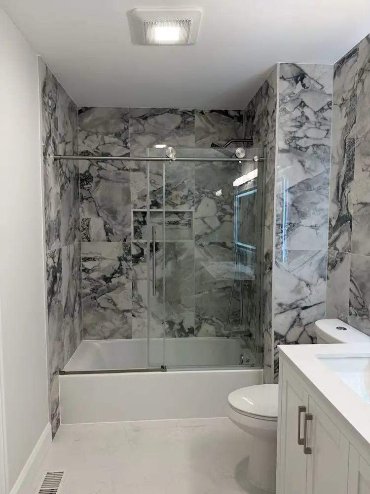Another view: Hall bathroom with bold marble-look porcelain, sliding glass tub door and double vanity with lighted mirror, Mentor, Ohio