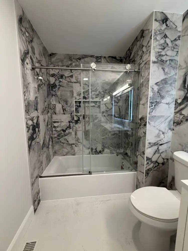 Another view: Hall bathroom with bold marble-look porcelain, sliding glass tub door and double vanity with lighted mirror, Mentor, Ohio