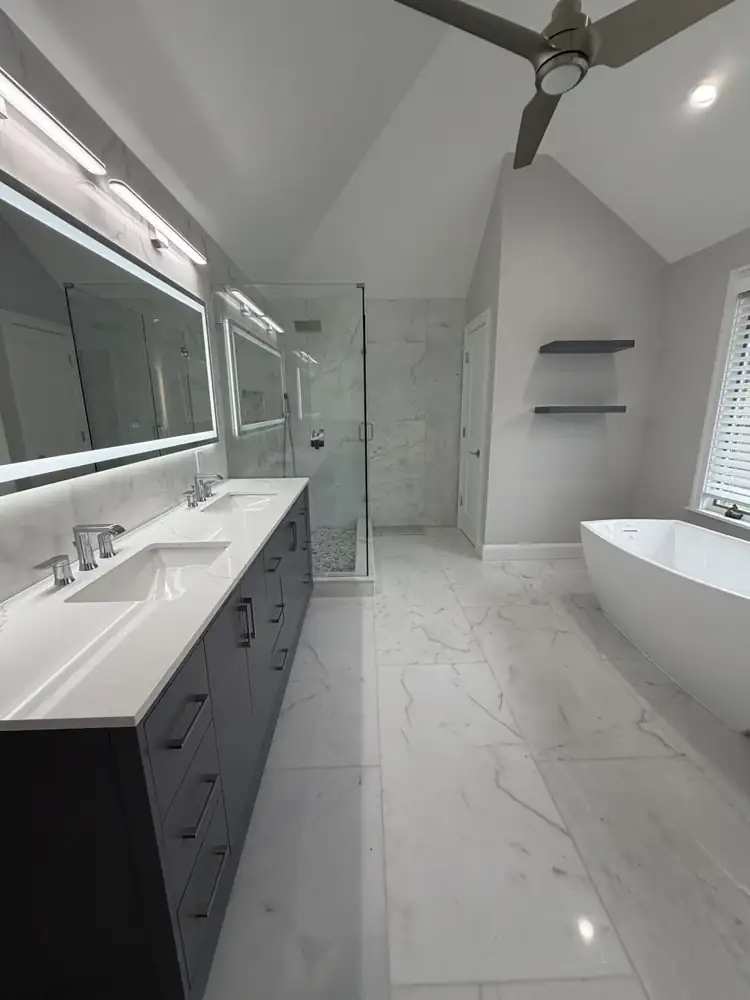Primary bathroom with freestanding tub, glass shower, gray double vanity and marble-look floor under a vaulted ceiling, Mentor, Ohio