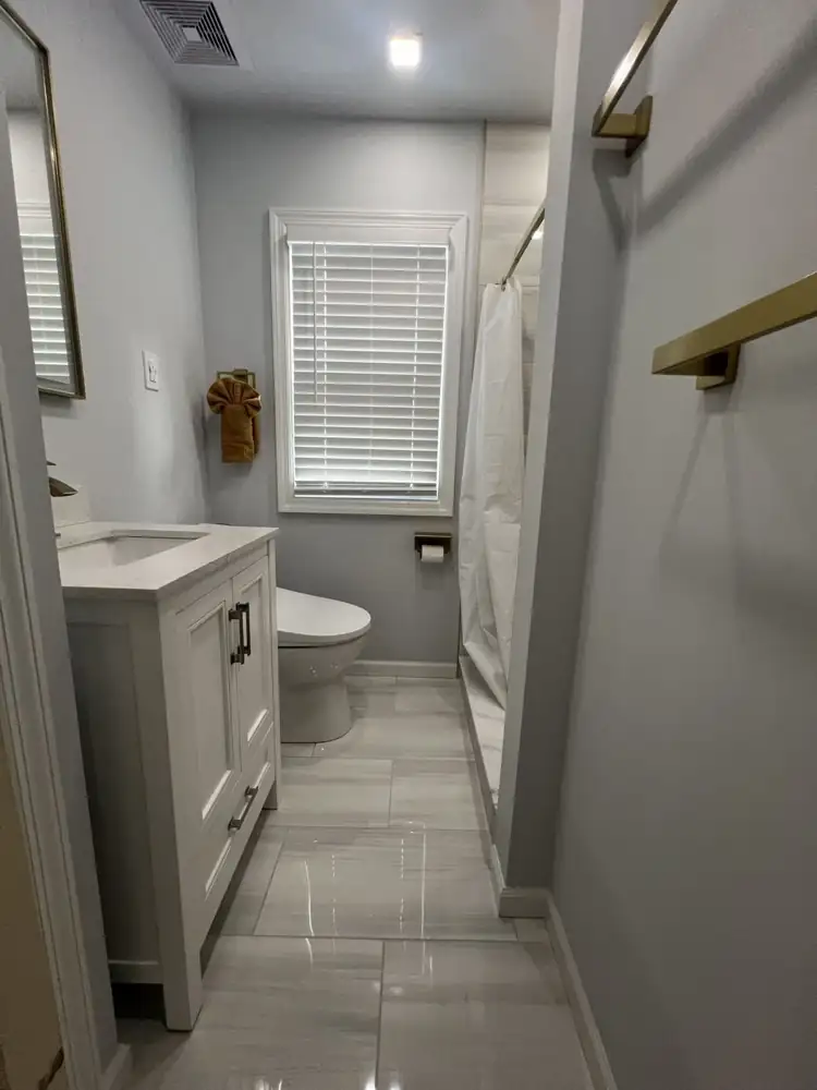 Small bathroom with white vanity, large-format gray porcelain floor, new window trim and brushed gold accessories, Mentor, Ohio