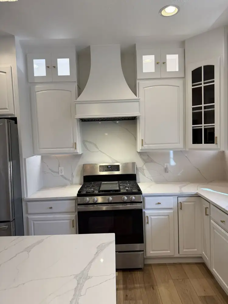 Custom curved range hood with full-height quartz backsplash and lit glass-front upper cabinets