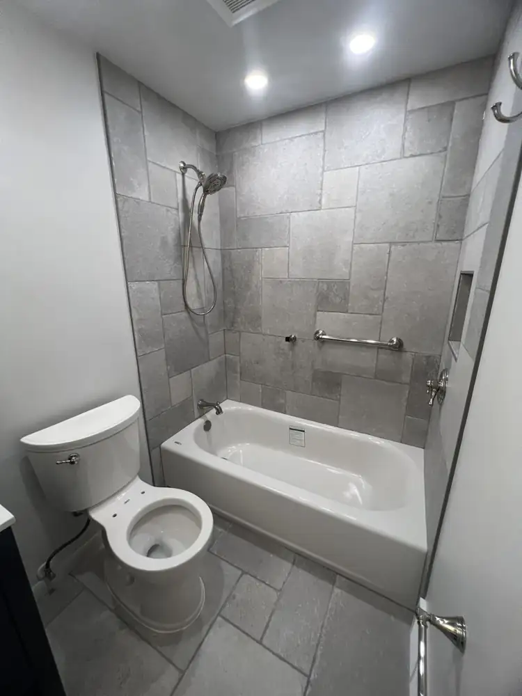 Hall bathroom with gray stone-look tile in a French pattern, new tub, niche and grab bar, Gates Mills, Ohio