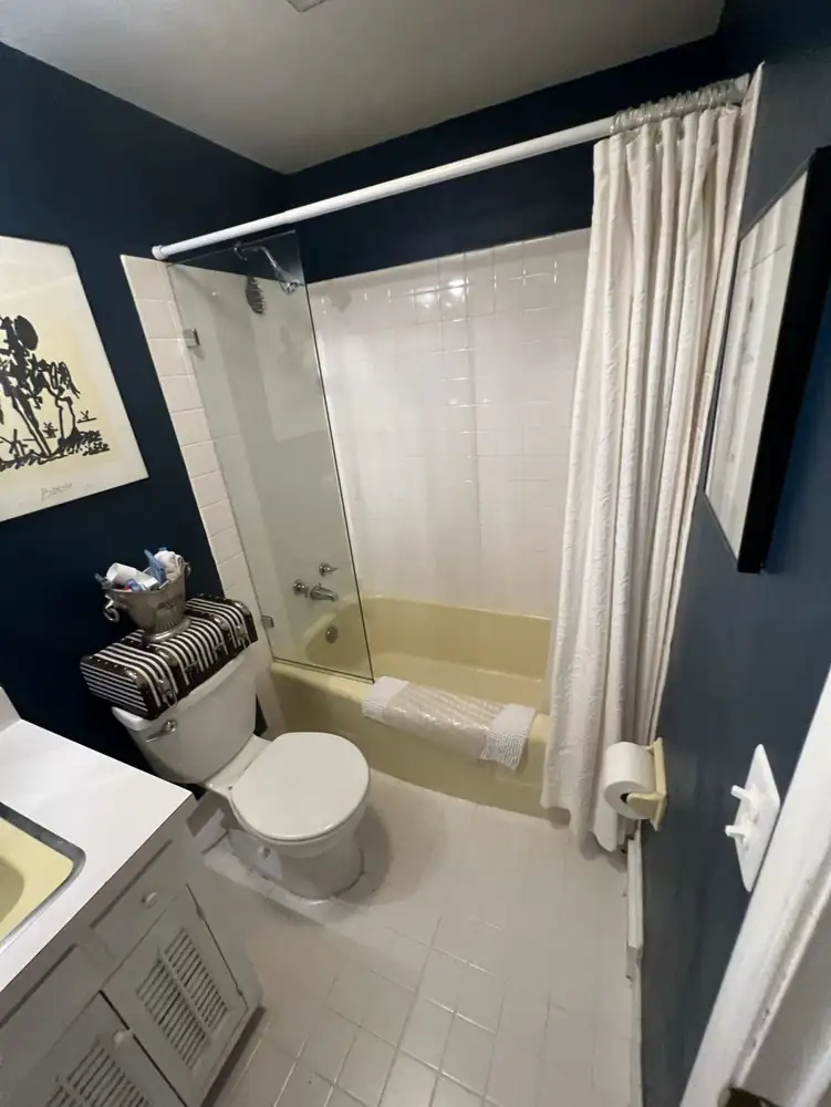 Hall bathroom with yellow tub, white square tile and shower curtain before remodel, Gates Mills, Ohio