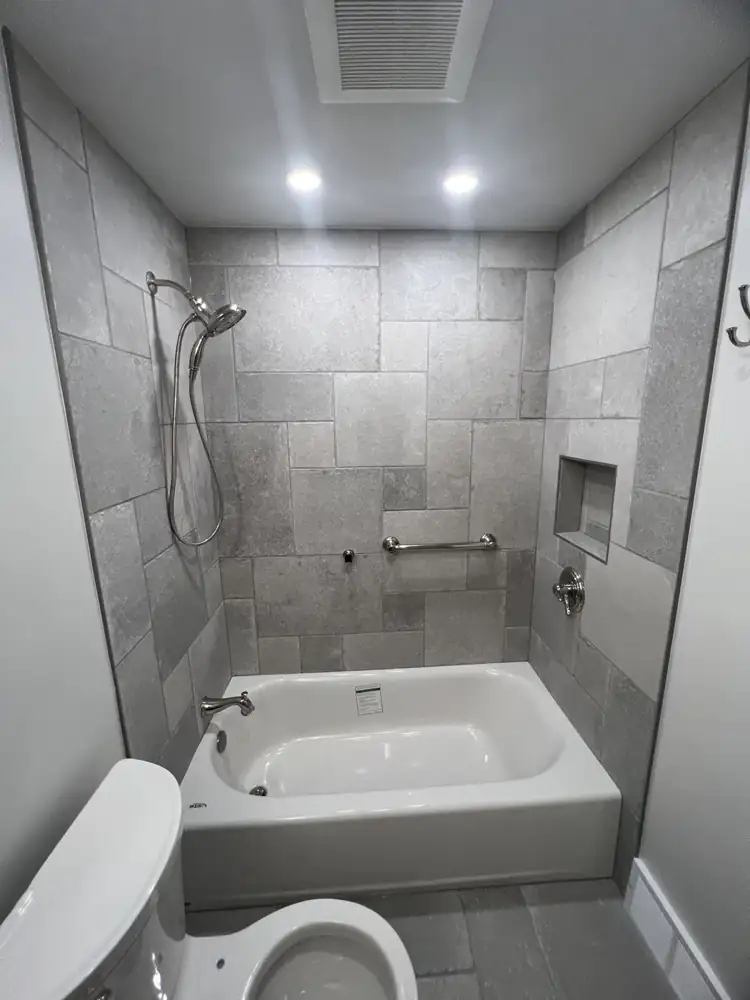 Updated hall bathroom with new tub, stone-look tile surround and gray tile floor, Gates Mills, Ohio