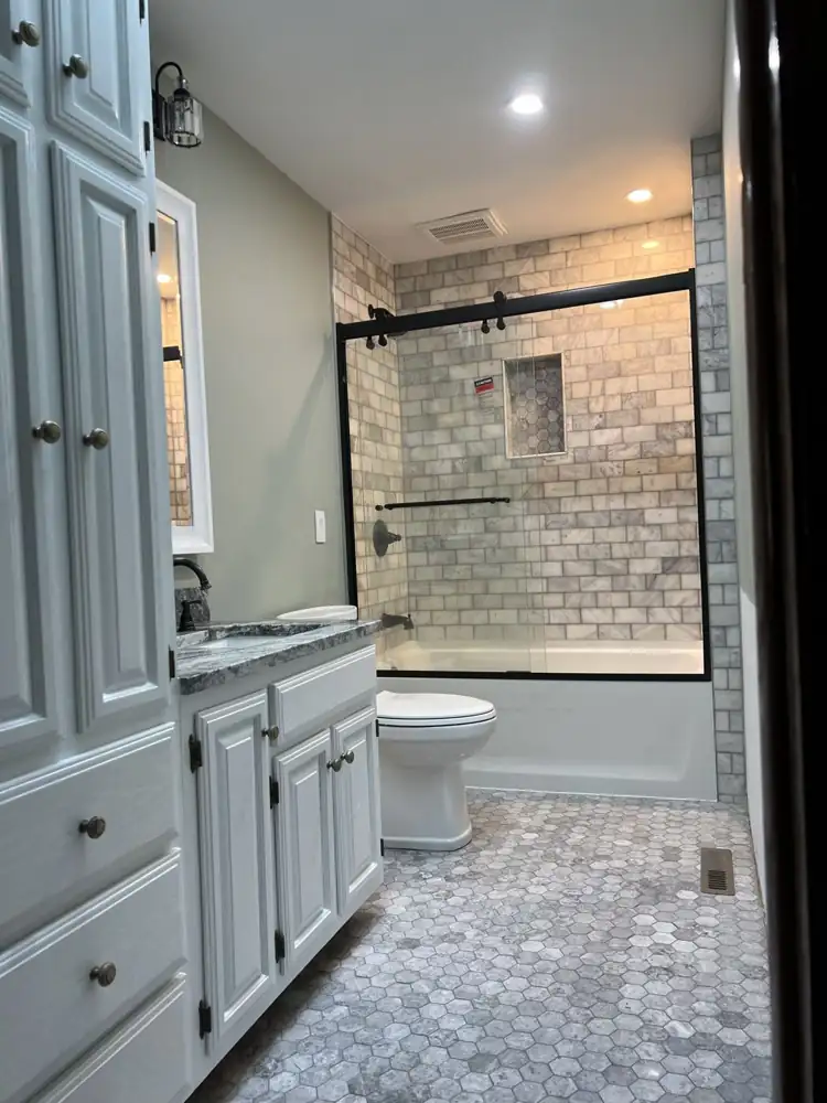 Hall bathroom with marble subway tile tub surround, black sliding glass door and hexagon marble floor, Northeast Ohio