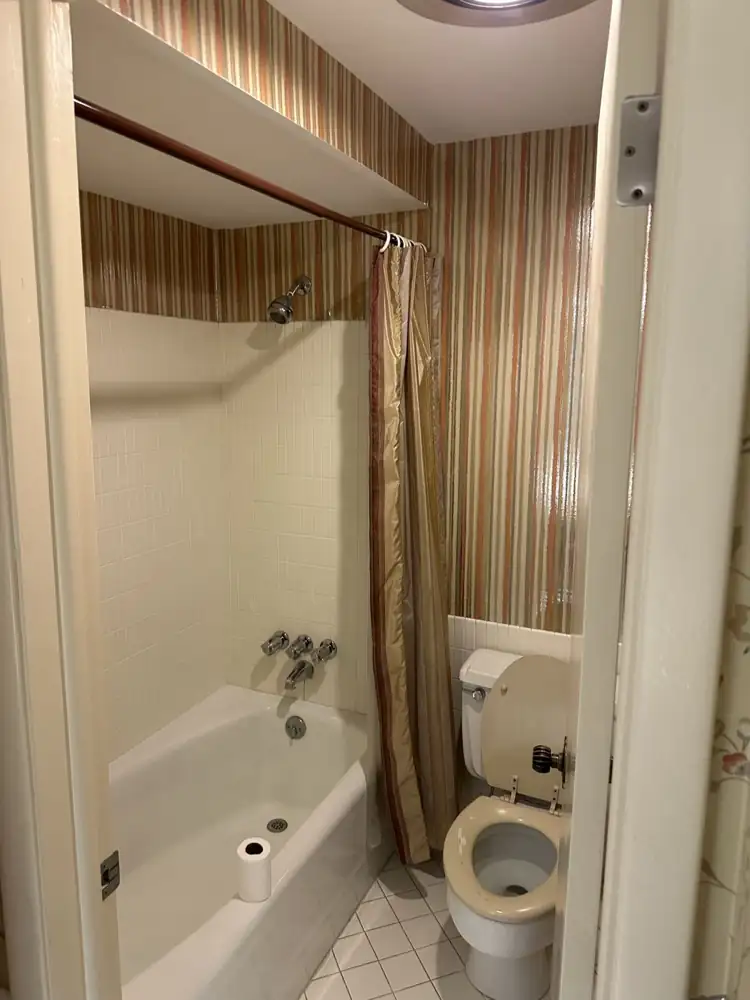 Small bathroom with striped wallpaper, old tub and shower curtain before remodel, Northeast Ohio