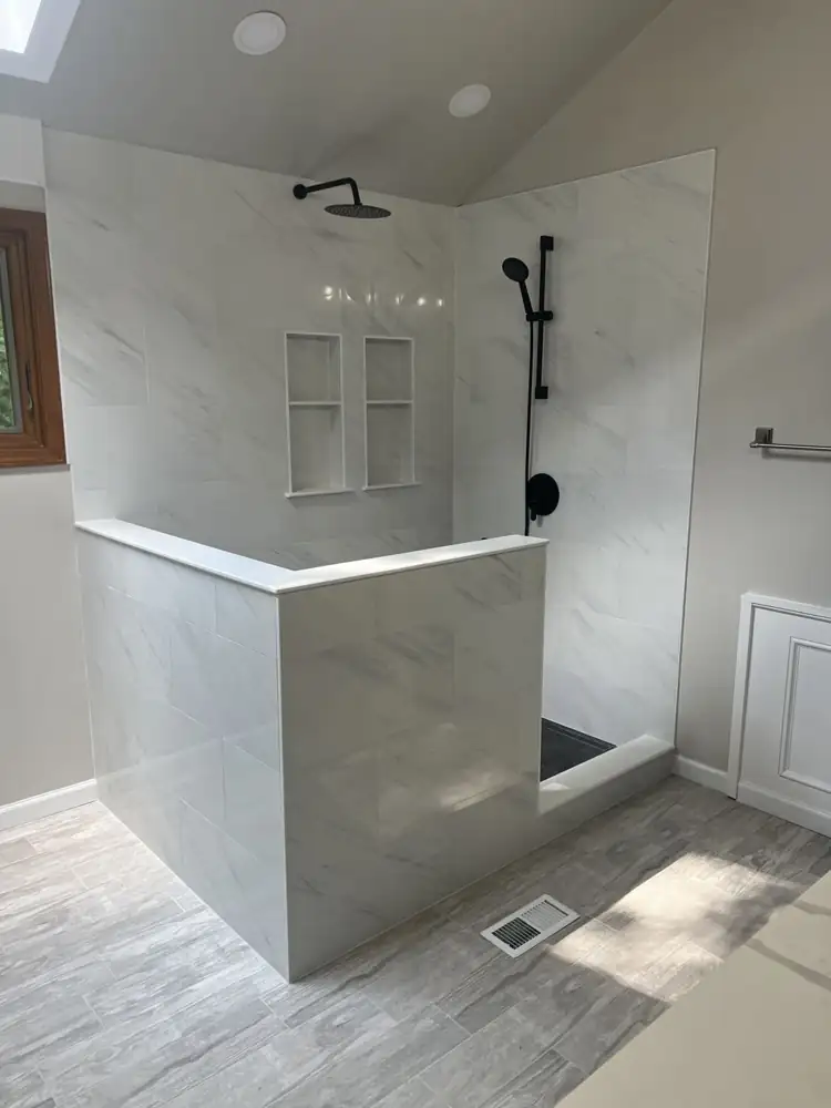 Walk-in shower with white marble-look porcelain, half wall with quartz cap, twin niches and matte black fixtures, Northeast Ohio
