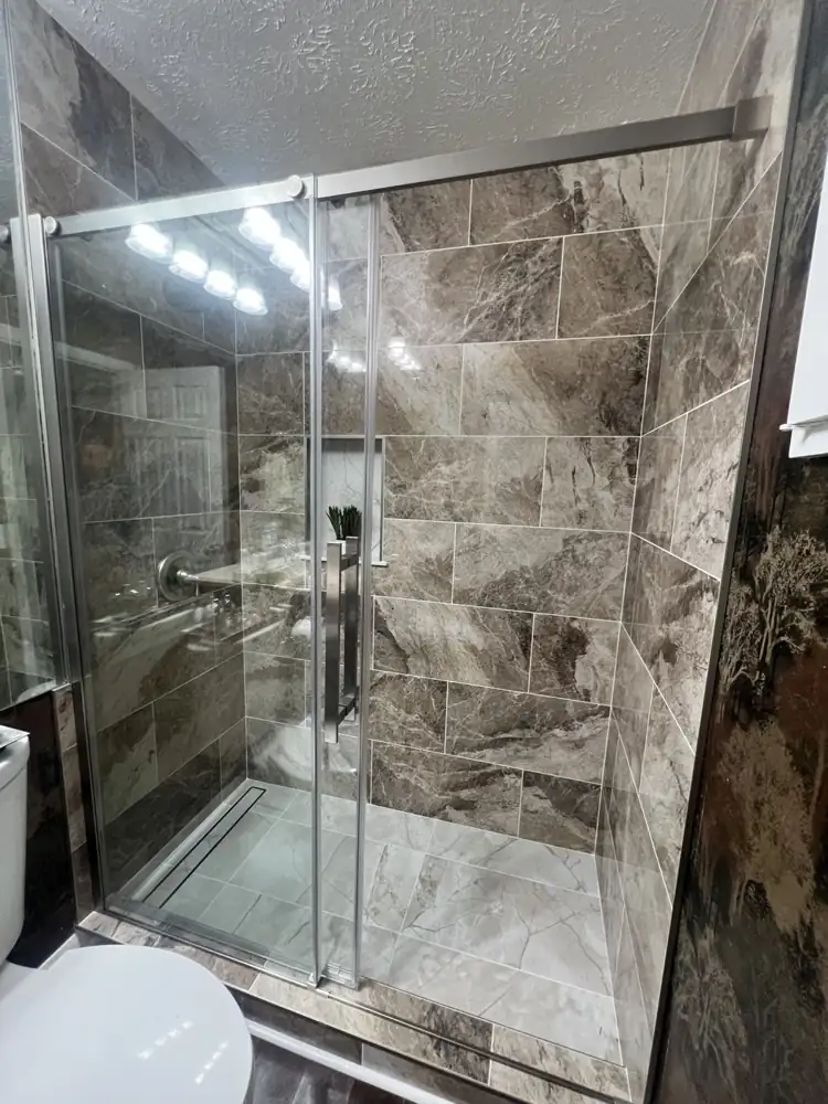 Tub-to-shower conversion with large-format brown marble-look tile and brushed nickel sliding door, Northeast Ohio
