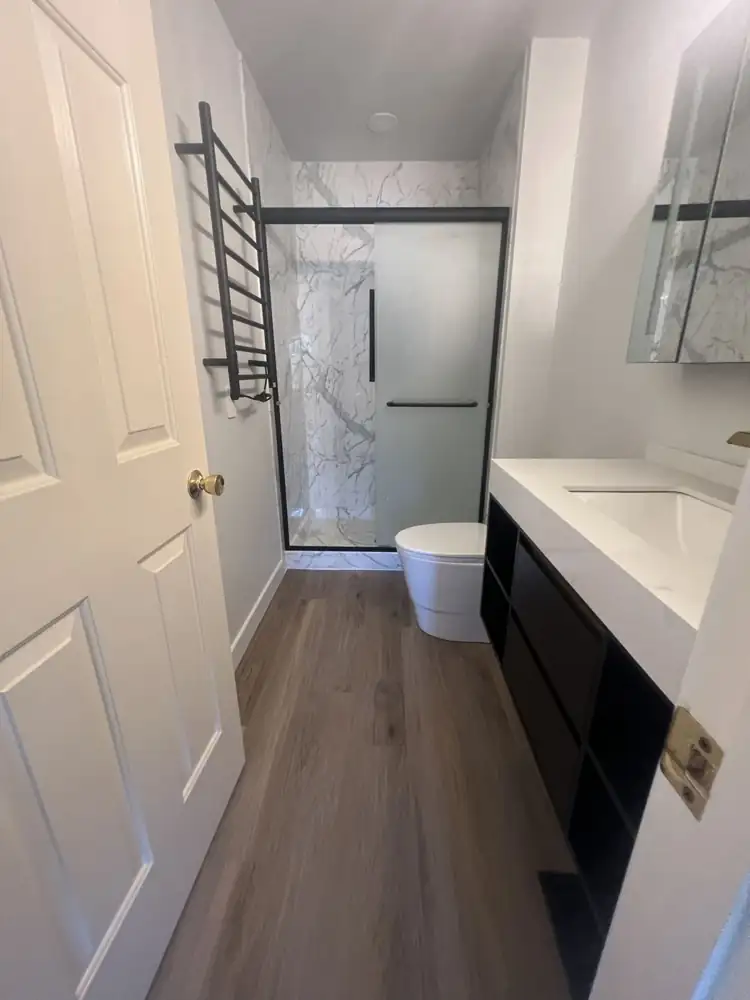 Bathroom with white marble-look shower walls, black sliding door, heated towel ladder and wood-look floor, Northeast Ohio
