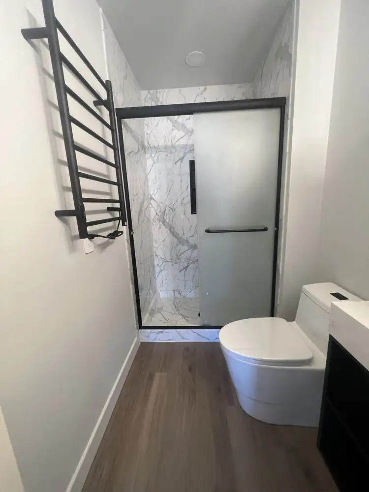 Marble-look shower with frosted sliding glass door, black towel warmer and modern toilet, Northeast Ohio