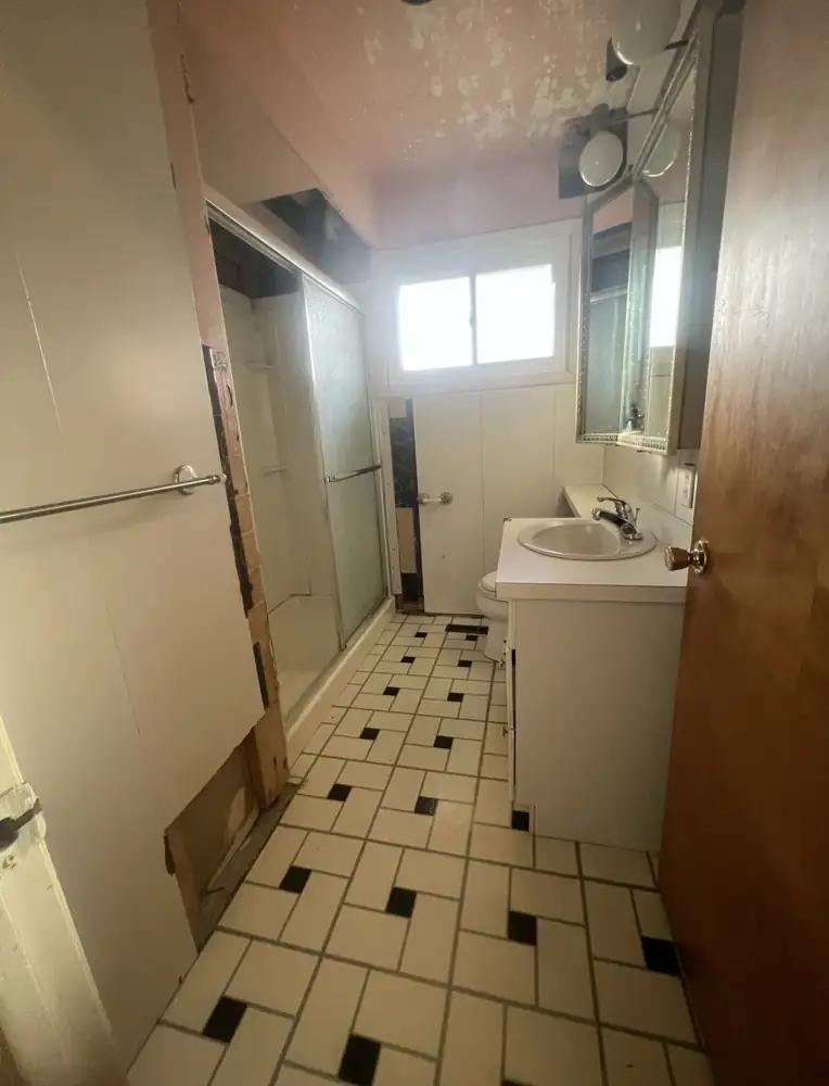 Worn bathroom with old sliding-door shower and damaged walls before remodel, Northeast Ohio