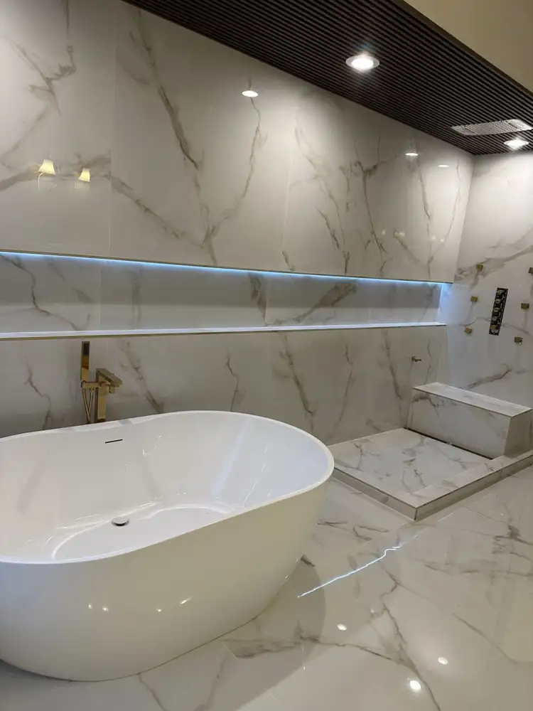 Freestanding tub with gold floor-mount filler beside a curbless marble shower with LED-lit niche, Northeast Ohio