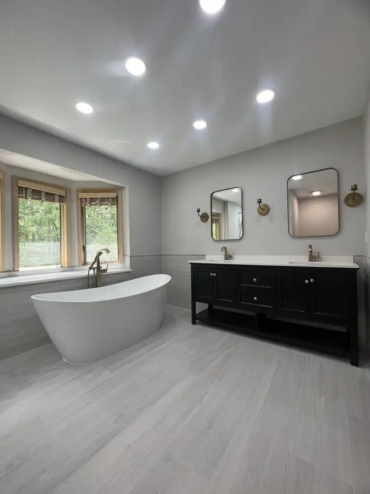Primary bathroom with freestanding tub under bay window, black double vanity and brushed gold fixtures, Northeast Ohio