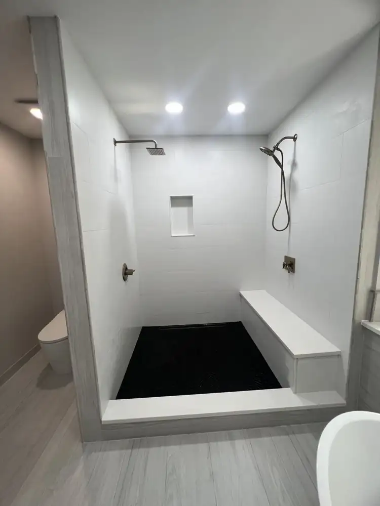Walk-in shower with white large-format tile, black herringbone floor and quartz bench