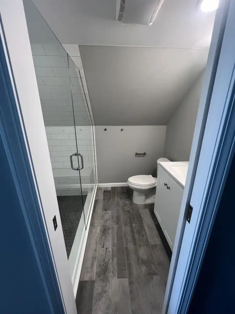 Attic bathroom with frameless glass shower following the sloped ceiling and gray wood-look tile floor, Northeast Ohio
