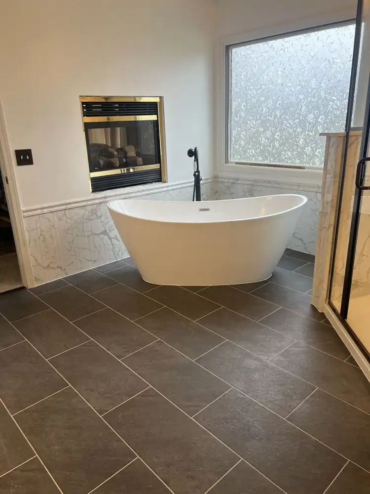 Freestanding tub with matte black floor-mount filler under a fireplace and frosted window, Northeast Ohio