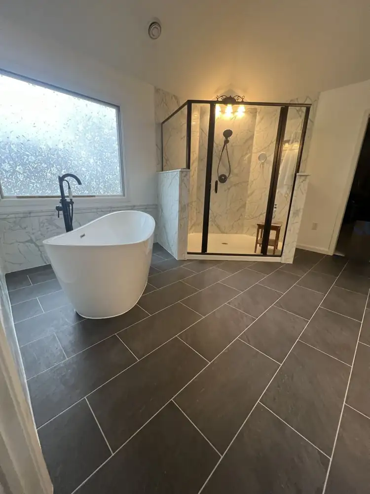 Freestanding tub and black-framed glass shower with marble-look walls on a charcoal tile floor, Northeast Ohio