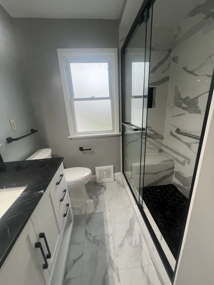 Bathroom with white marble-look porcelain, black hexagon shower floor, sliding glass door and black marble vanity top, Northeast Ohio