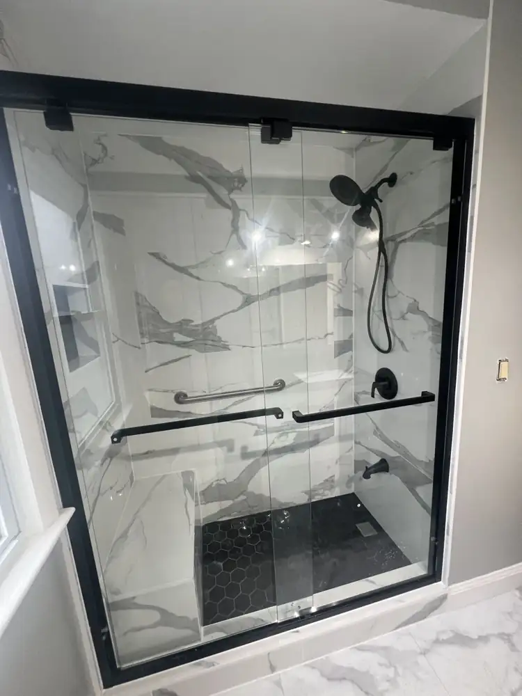 Black-framed sliding glass shower door with marble-look porcelain and black hex mosaic floor, Northeast Ohio