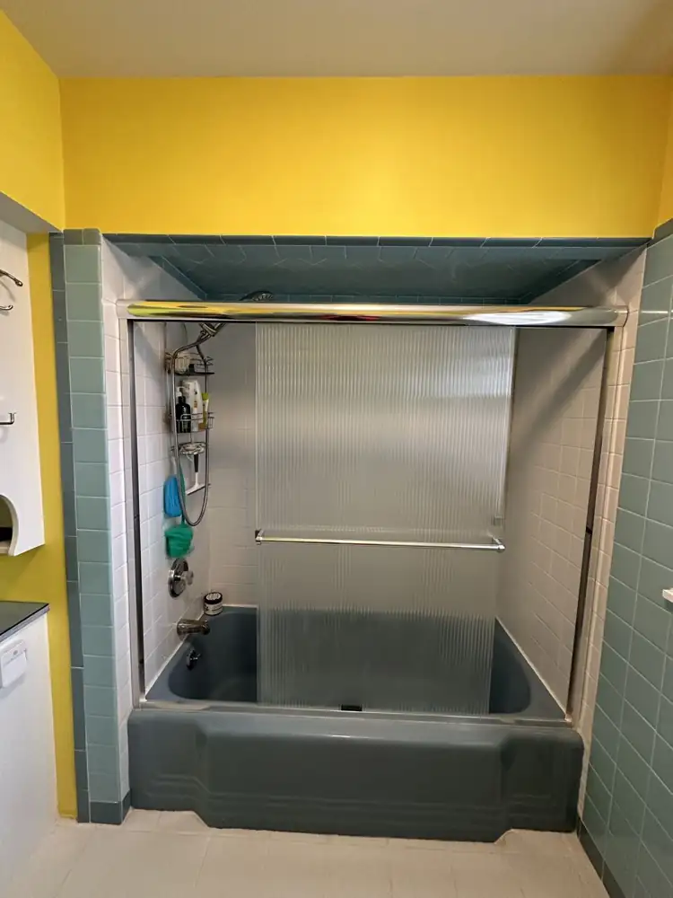 Vintage bathroom with blue tub, sliding glass doors, teal tile and yellow walls before remodel, Northeast Ohio