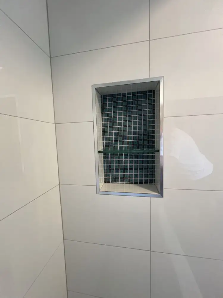 Shower niche lined with blue mosaic tile, glass shelf and brushed metal trim, Northeast Ohio