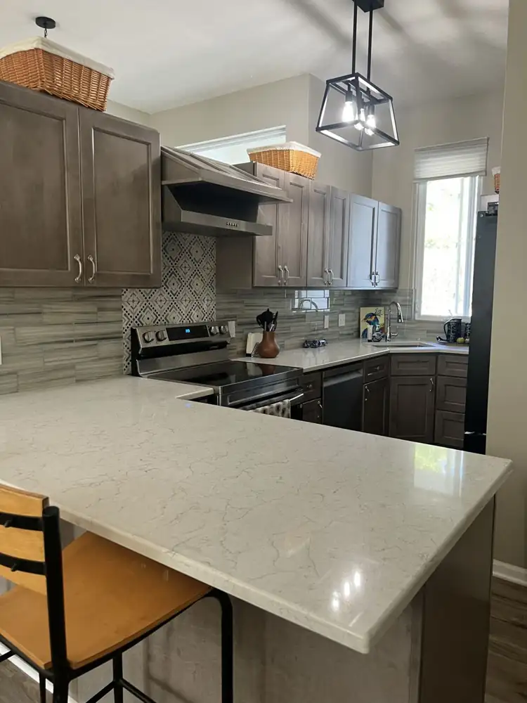 Quartz peninsula with gray shaker cabinets, patterned tile accent behind the range and stainless hood, Northeast Ohio