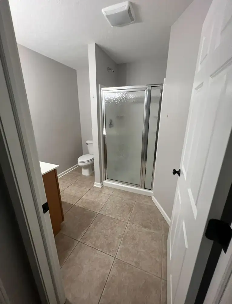 Bathroom with framed glass shower stall and beige tile floor before remodel, Northeast Ohio