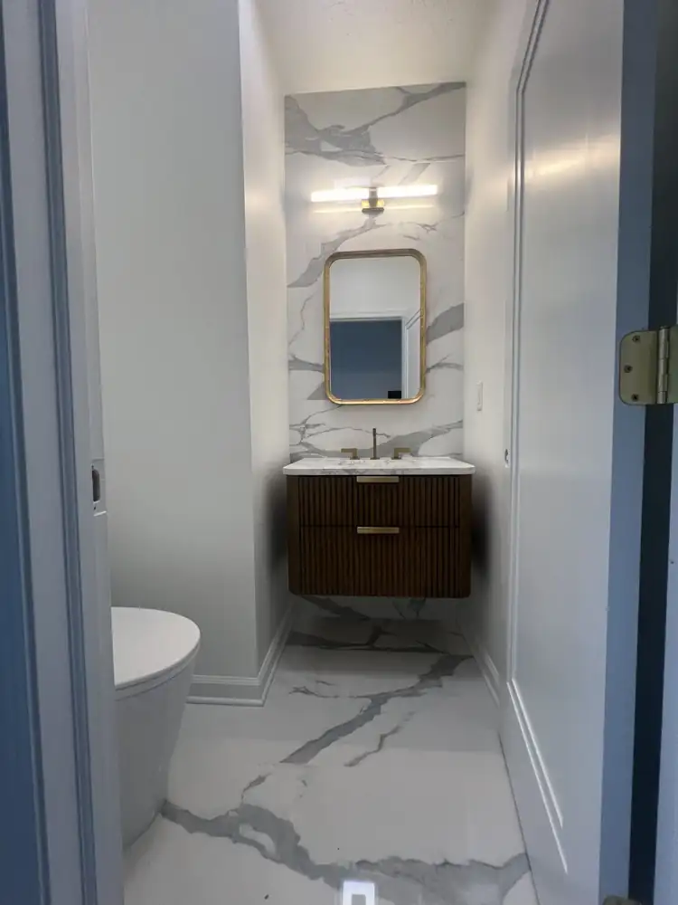 Powder room with marble-look porcelain wall and floor, fluted walnut vanity and brass fixtures