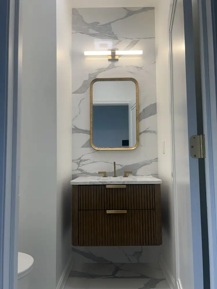 Fluted wood floating vanity with gold mirror, brass faucet and marble-look slab wall, Northeast Ohio
