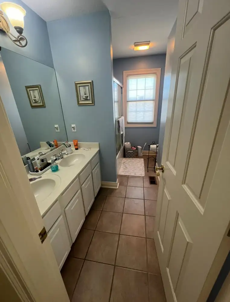 Hall bathroom with white double vanity, blue walls and brown tile floor before remodel, Northeast Ohio