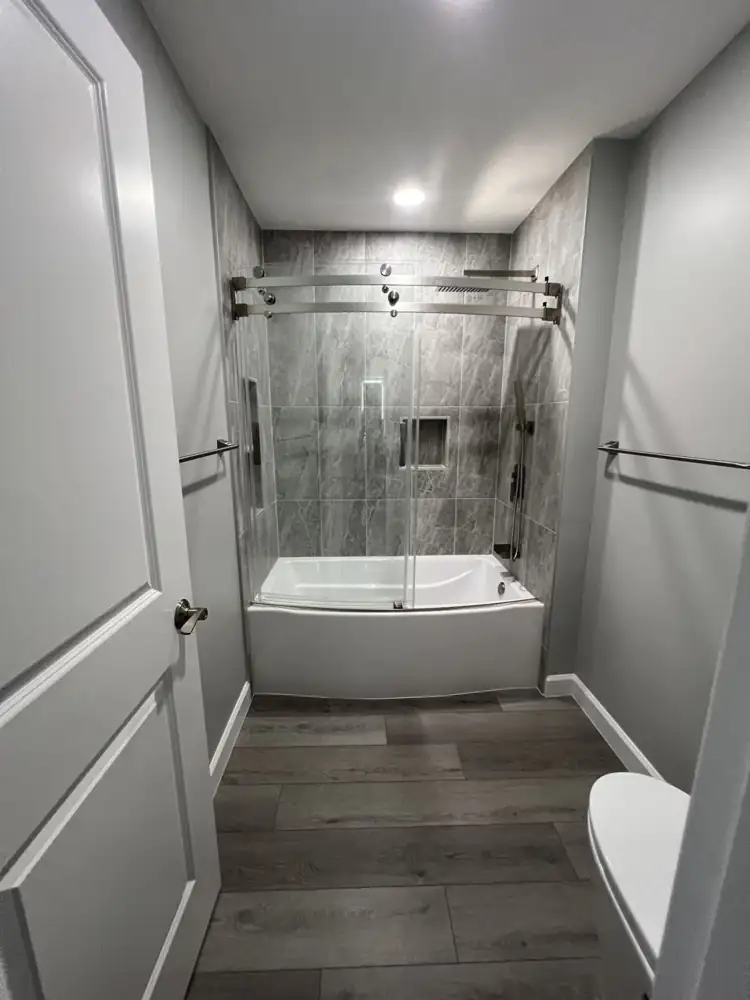 Bathroom with gray stone-look porcelain tub surround, frameless sliding glass doors and plank floor, Northeast Ohio