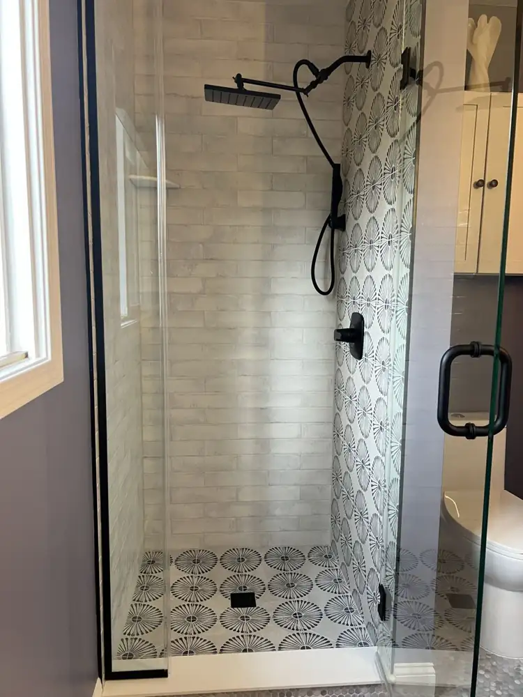 Walk-in shower with white brick-look tile, black-and-white daisy pattern tile wall and floor, and black rain shower, Northeast Ohio