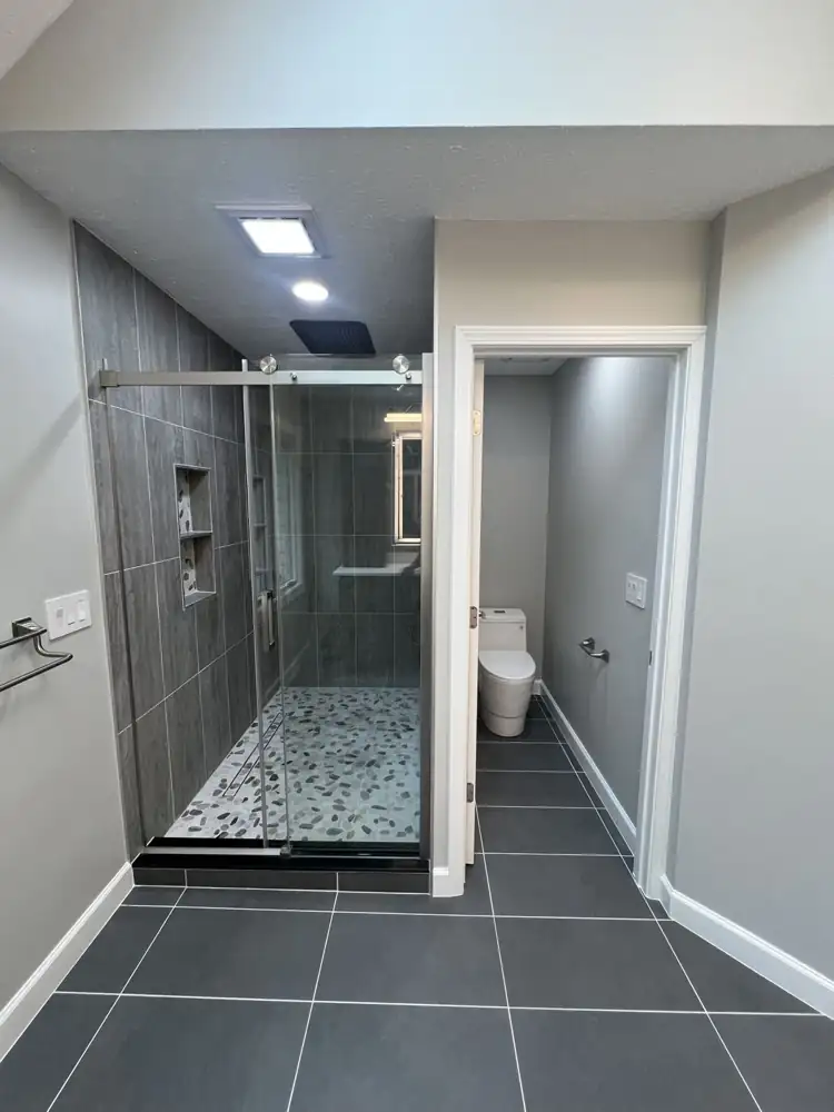 Primary bathroom with large charcoal floor tile, frameless sliding glass shower, river pebble floor and private toilet room, Northeast Ohio