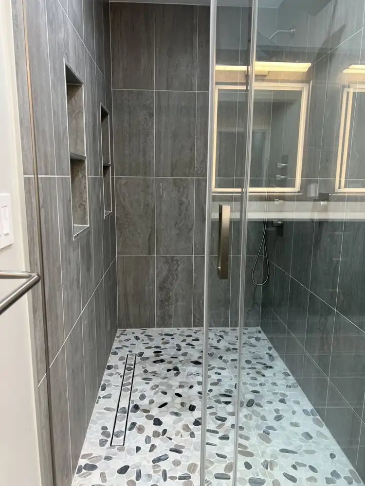 Walk-in shower with gray travertine-look tile, river pebble floor, linear drain and double niches, Northeast Ohio