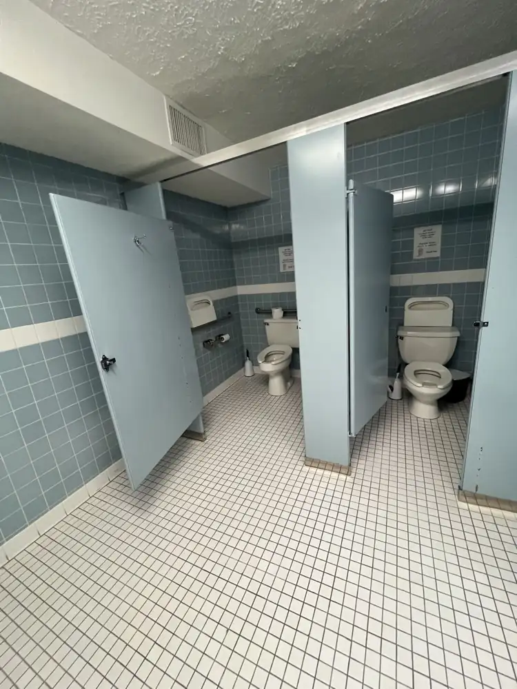 Commercial restroom with blue wall tile, small white floor tile and old stall partitions before renovation, Northeast Ohio